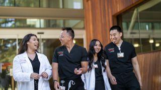 Photo shows four Nursing students at Pacific's School of Health Sciences talking and smiling while walking out of the nursing classroom.